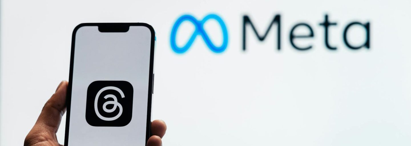 holding a smartphone with the threads app with the meta platforms logo in the background
